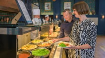 A guest piles peas onto her plate at the Market Kitchen hot buffet counter