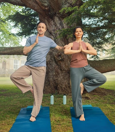 A couple doing yoga, the man using the woman as a support, on the grounds at Heythrop Park