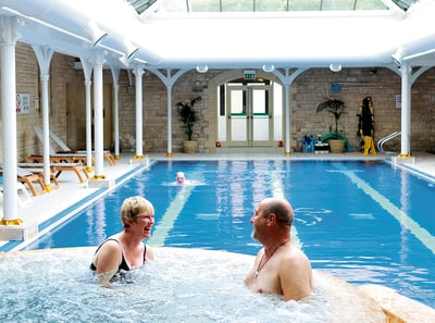 Two guests enjoying the bubble pool at Thoresby Hall Hotel, whilst another guest is swimming in the pool behind