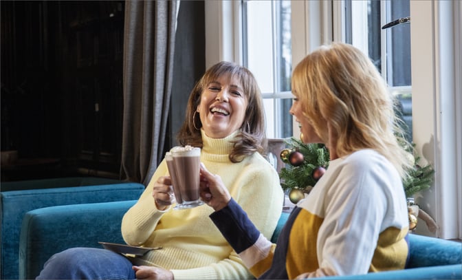 Two women enjoying a festive moment on a couch, each holding a drink, radiating happiness and friendship.